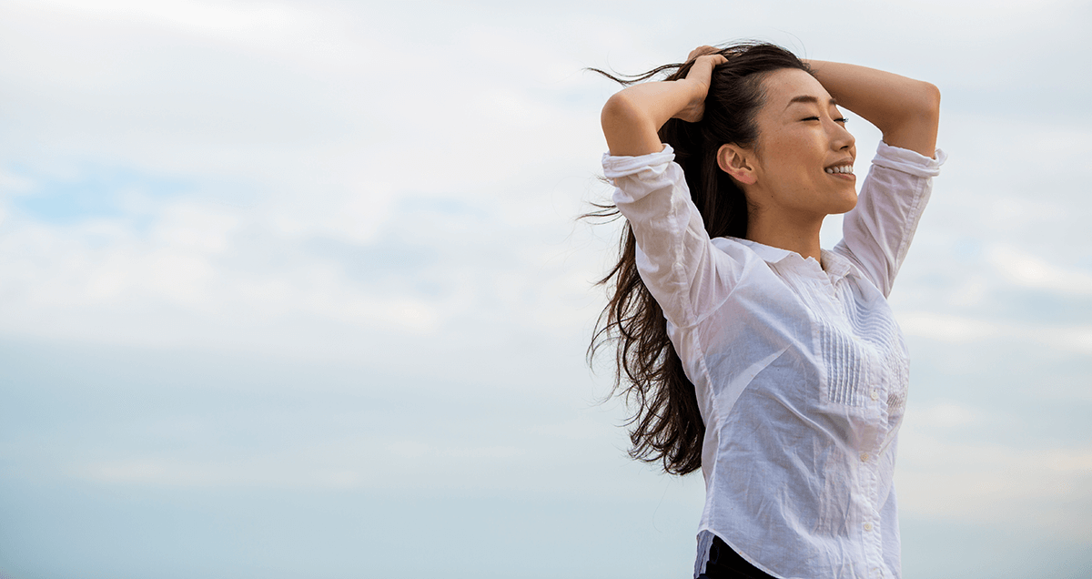Smiling Asian woman with her eyes closed with a sky in the background.