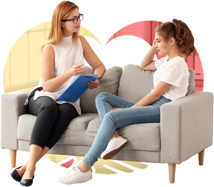 A girl sitting with a therapist while the therapist takes notes and speaks to the girl.