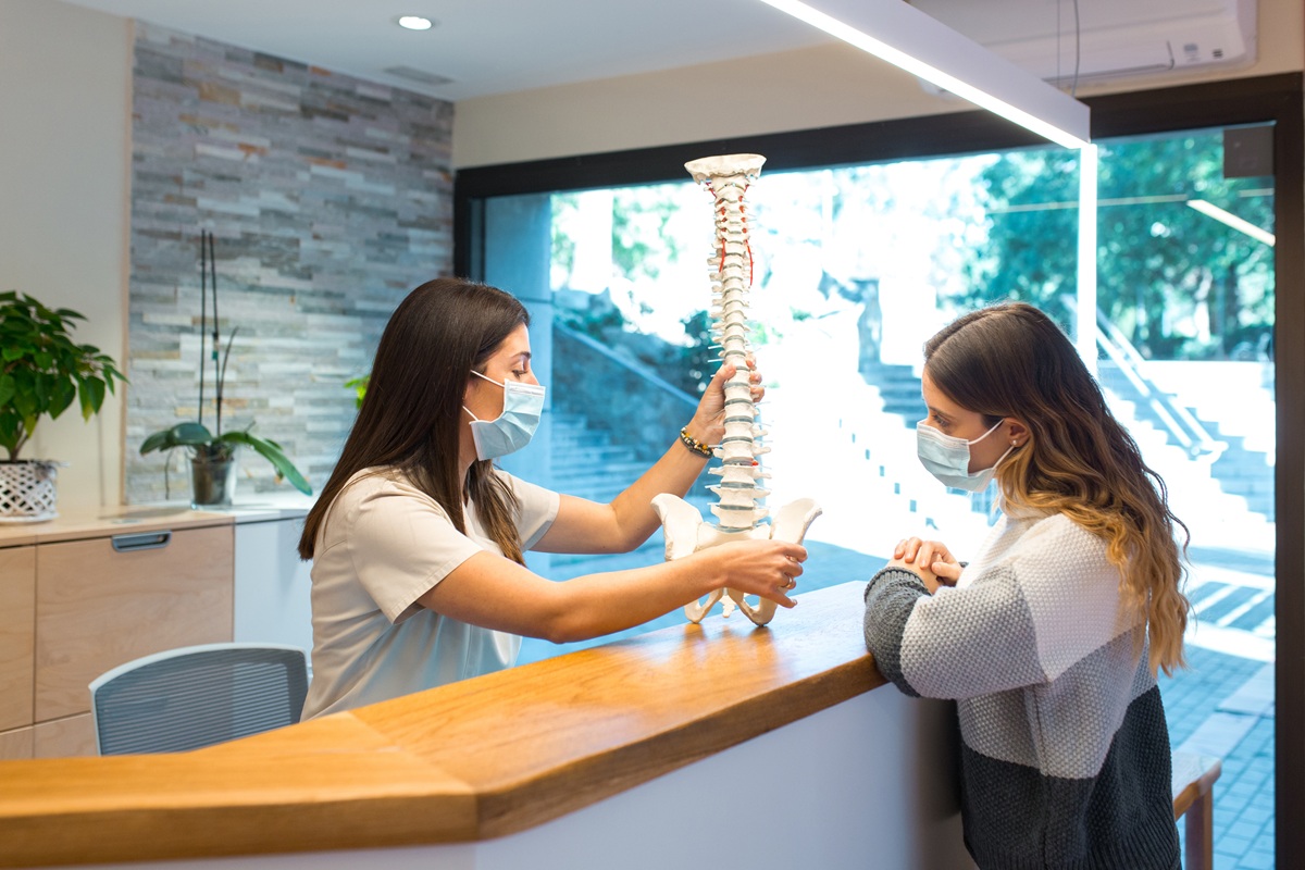 Female physiotherapist explaining spine model to a patient during a consultation.